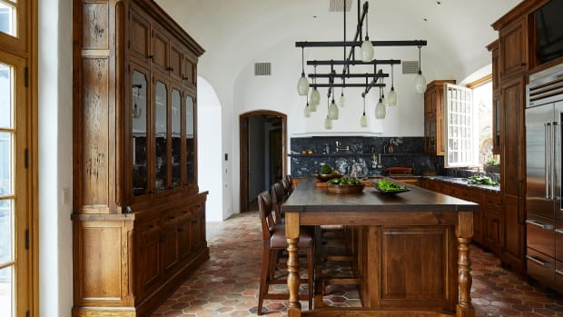 In the kitchen, the central island, made of reclaimed oak and topped with walnut, is illuminated by a contemporary custom light fixture. The backsplash is paneled with slabs of Titanium black marble. Photos by William Abranowicz