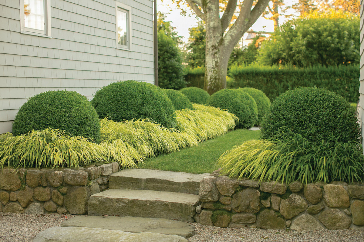 Both the garage and the house are hemmed neatly in a skirt of variegated hakonechloa ornamental grass punctuated by immaculately clipped boxwood orbs.